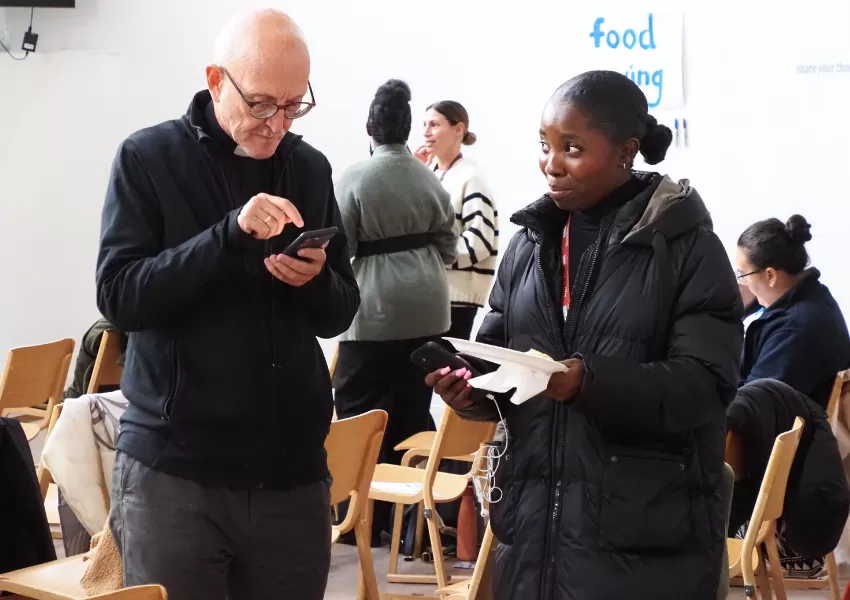 guests networking in between presentations, man looking something up in his phone while a woman smiles at him