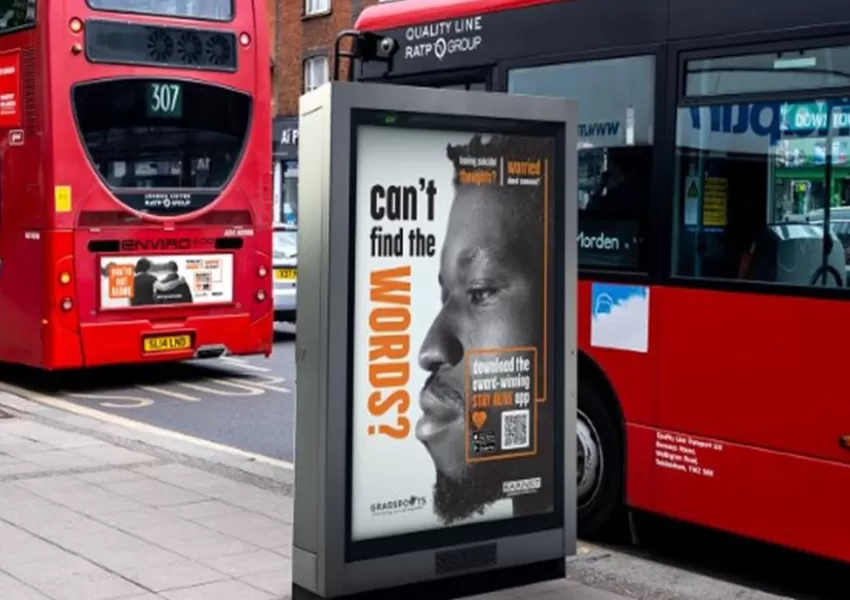 An on-street advertising display board featuring the stay alive campaign ('can't find the words?' + the side profile of a man's face), with two red London in the background