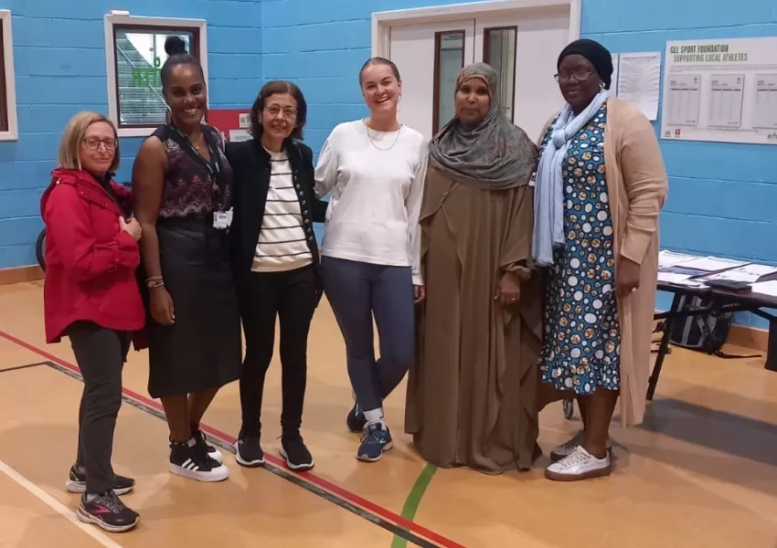 A group shot of 6 women in the gym, all stood together in a row and smiling to camera