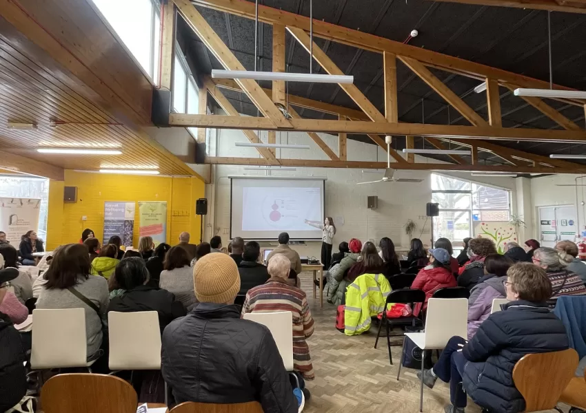 Picture of group listening to a female speaker delivering a presentation.