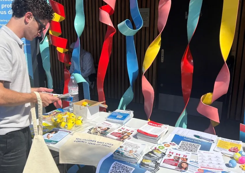 Person at a stall holding a totebag and looking at the vaccination information provided.