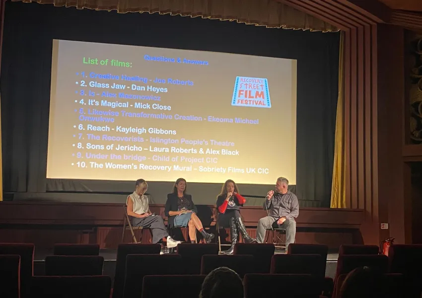 Four people sat on a stage in front of a cinema screen
