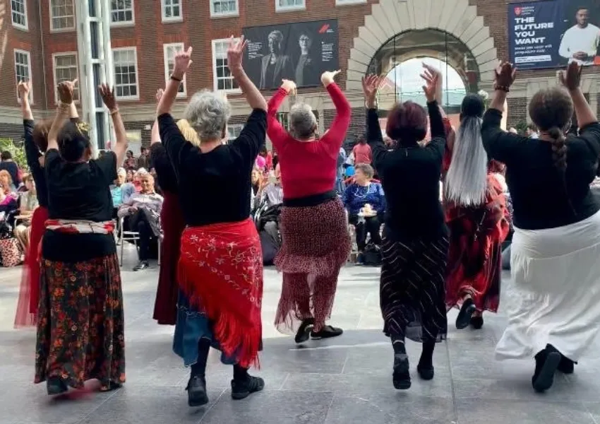 Older people dancing with arms in the air (photo taken from behind) in a performance to crowds at Silver Sunday 2025 event