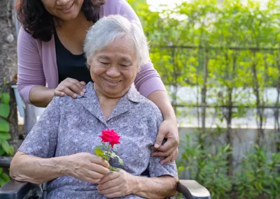 Old woman in wheelchair holding red flower and smiling