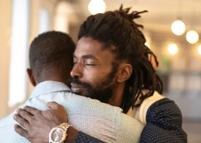 two men hugging, one with his face towards camera, one facing away