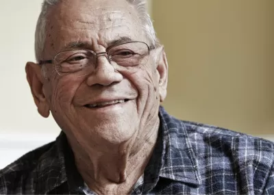 Older man smiling to camera, wearing a checkered shirt and glasses