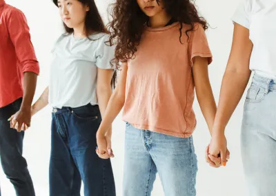 young people, with 2 young women in the middle, of various ethnicities holding hands in a chain