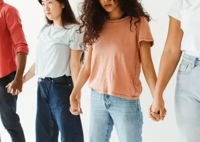 young people, with 2 young women in the middle, of various ethnicities holding hands in a chain