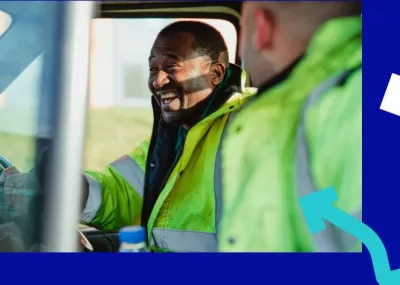 Two men in high vis jackets, sitting in a vehicle, laughing together