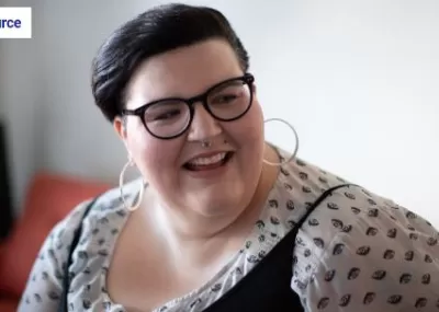 Plus size woman with short brown hair, smiling, wearing dotty blowse and black glasses