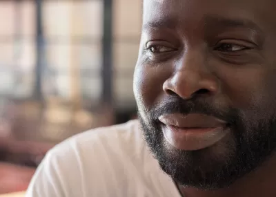 Close up of a man smiling softly, looking camera left, with a beard and wearing a white t-shirt.