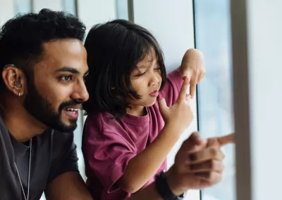 Man smiling and pointing out a window, with a small child