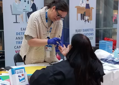 Picture of a healthcare professional performing a finger prick blood test for a local resident.