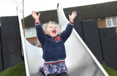 Small girl going down slide, smiling with arms in air